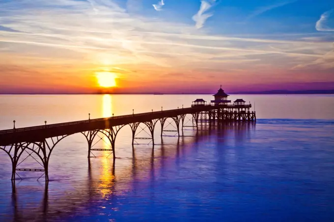 England, Somerset, Clevedon. The sun sets over the Bristol Channel behind the pier at Clevedon in Somerset.