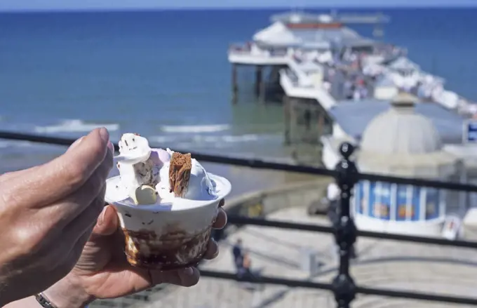 England, Norfolk, Cromer. Enjoying an ice cream overlooking Cromer pier.