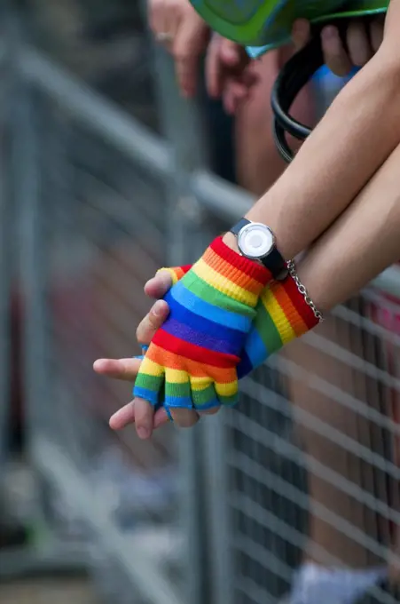 England, London. A gay couple holding hands wearing rainbow coloured fingerless mittens at the annual Pride London celebrations.