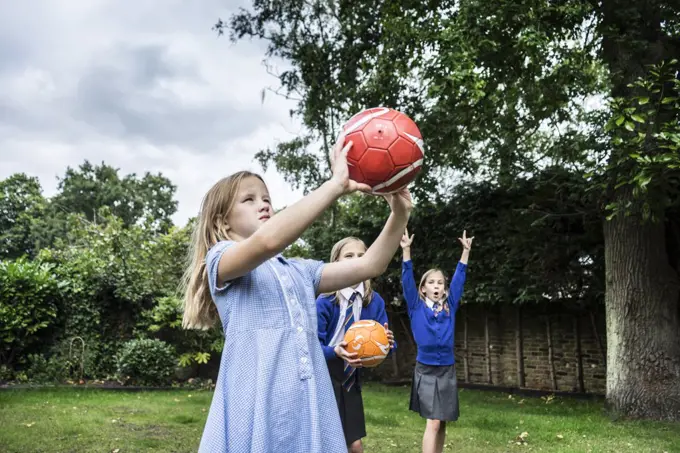 Three girls in school uniform playing with footballs outside.