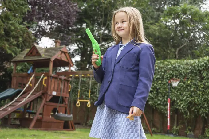 A ten year old girl in school uniform holding a water pistol.