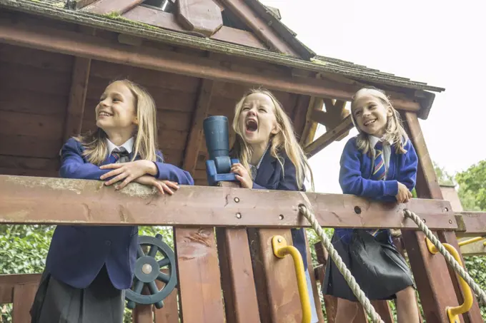 Three girls in school uniform stand together on wooden playground apparatus.