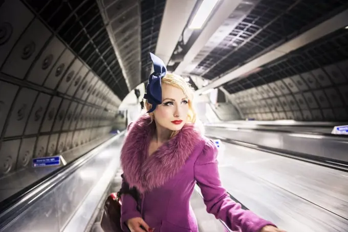 A stylish young woman dressed in 1930s style clothing on a London Underground escalator.