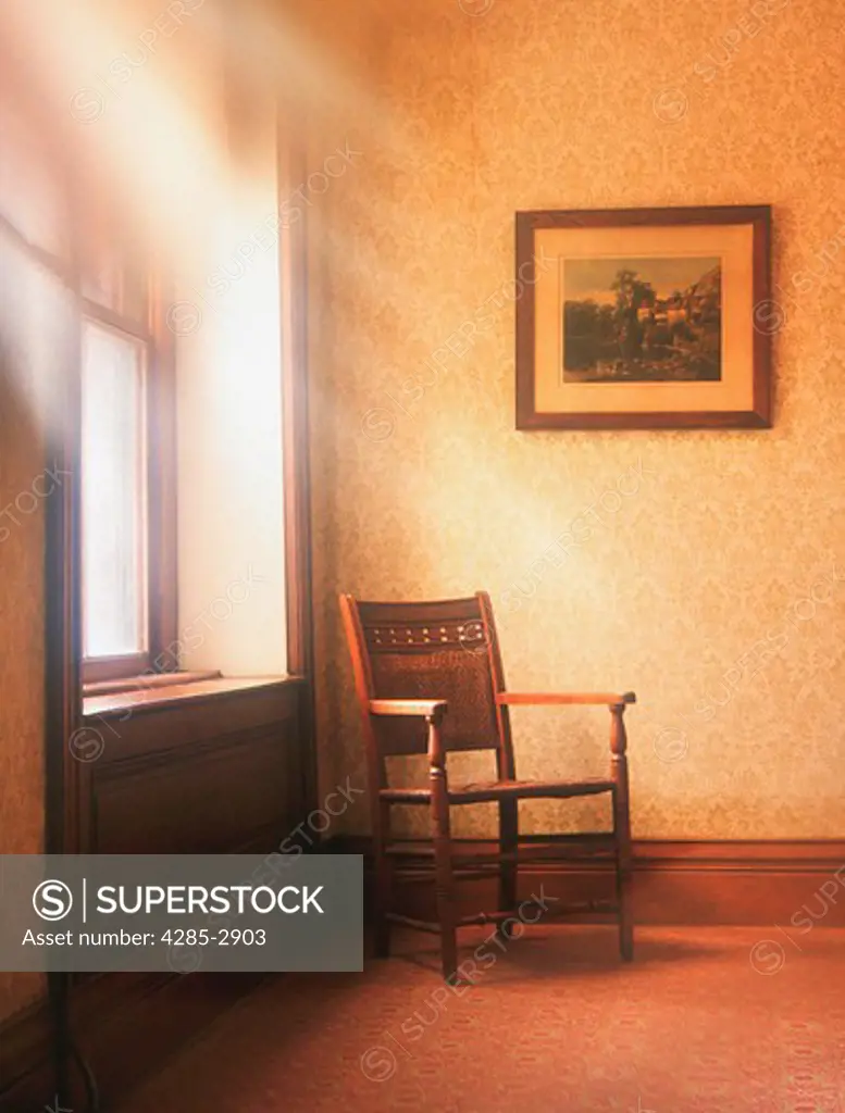 Sun rays coming in a house window shining down on a single chair.