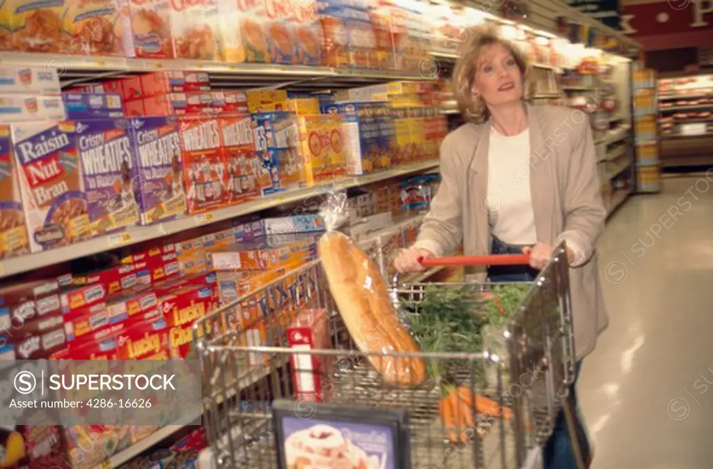A woman pushing a grocery cart in the aisle of a grocery store.
