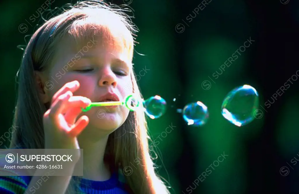 A young girl blowing bubbles with a bubble wand.