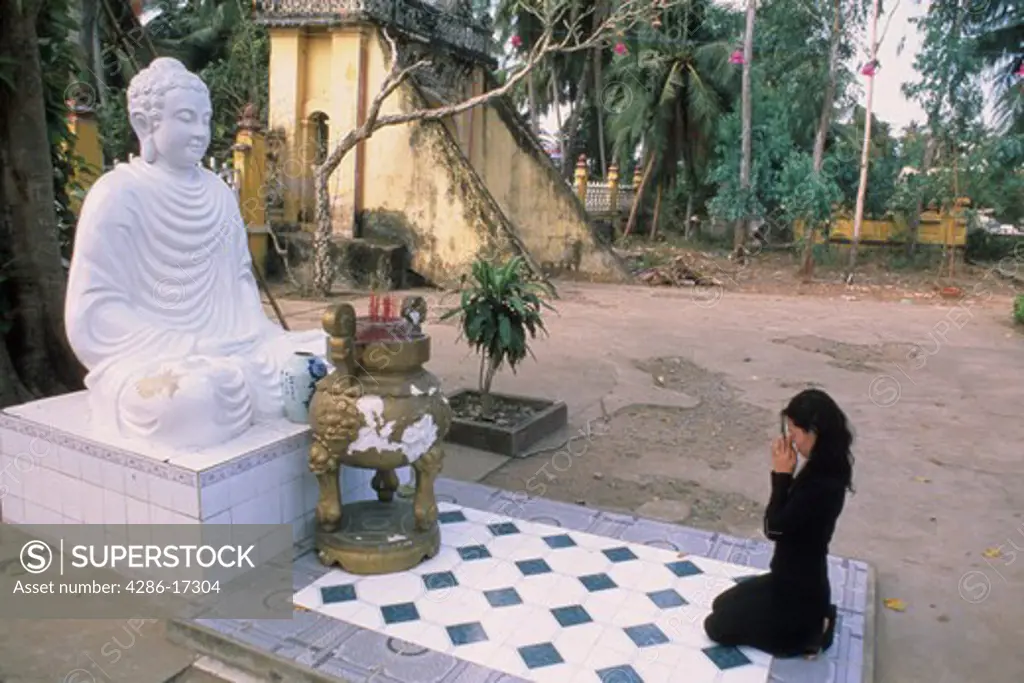 Woman kneeling bfore a Buddha statue and praying in Vietnam. 