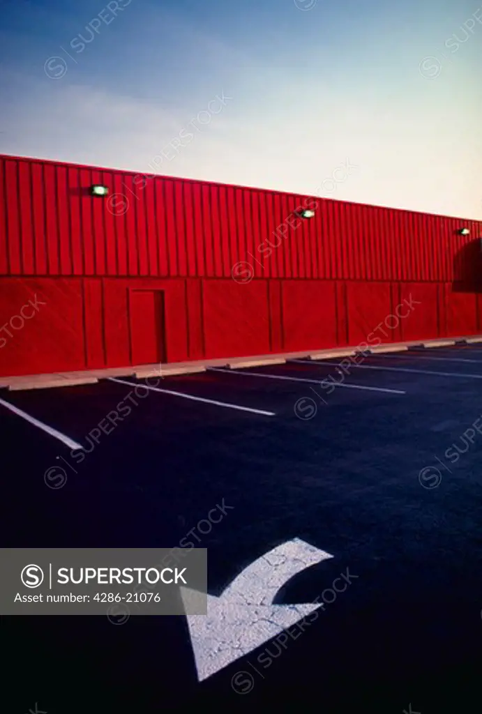 Directional arrow and parking spaces in a parking lot with a red store wall in the background.