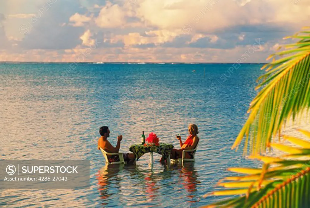 Couple sitting at table sharing sunset drink in Aitutaki lagoon