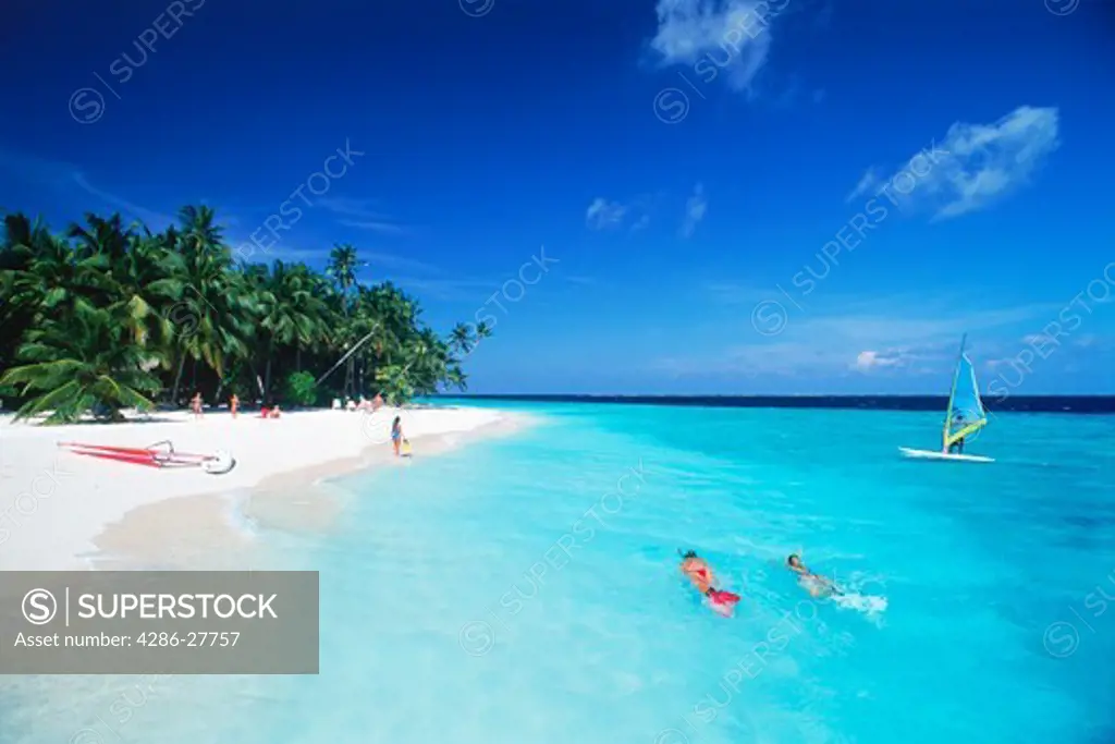 Couple snorkling in aqua waters with windsurfer at Fihalhohi Island in Maldives