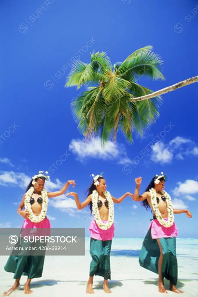 Three Polynesian girls with grass skirts and flower leis on Aitutaki Island in South Pacific