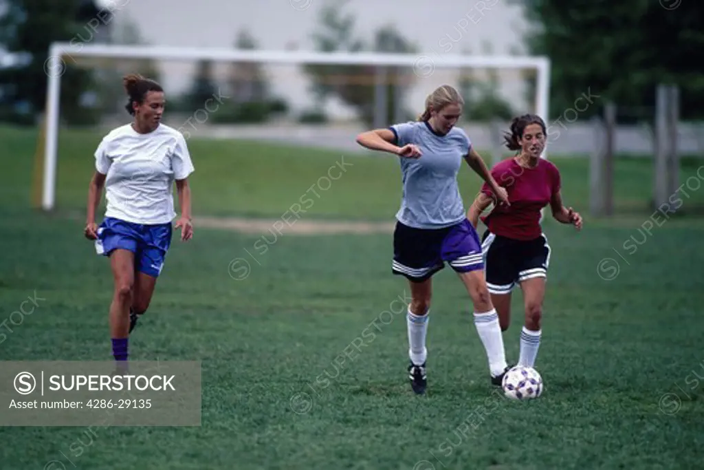 Three teenage girls energetically playing soccer.