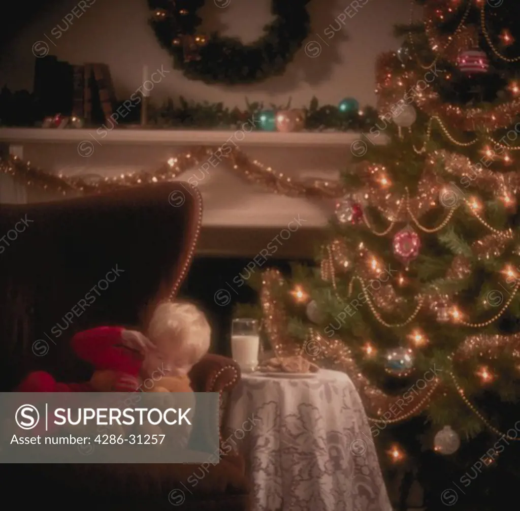 Young boy sleeping next to Christmas tree waiting for Santa Claus.