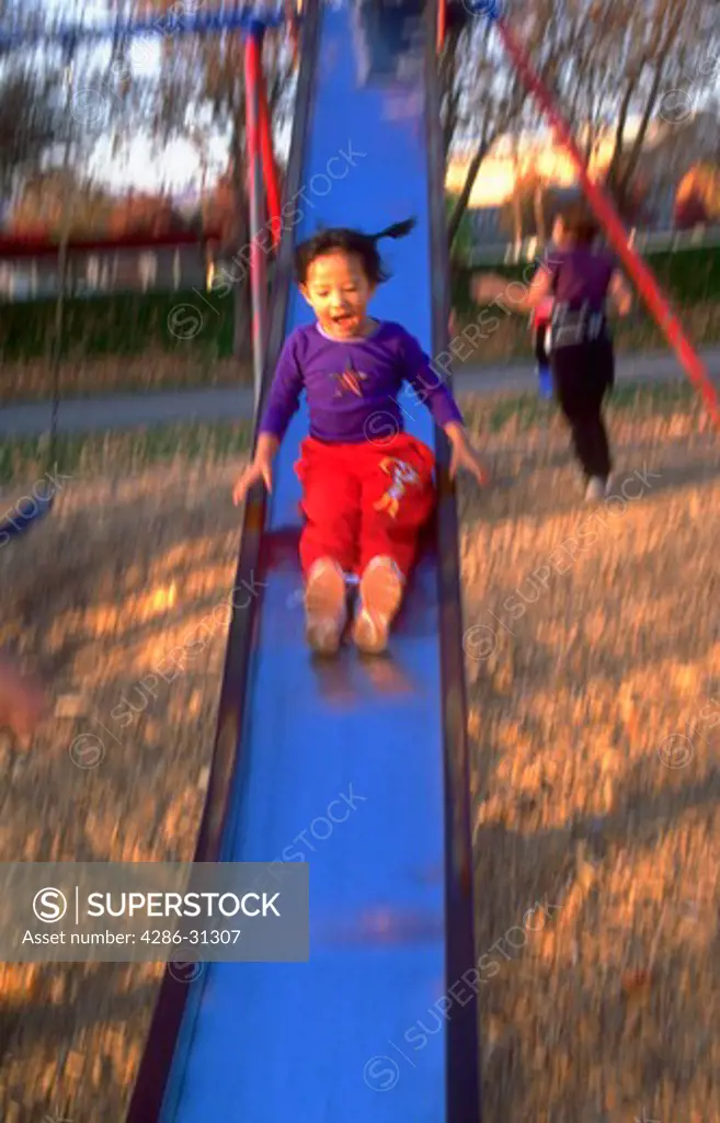 Young Asian girl screams with delight as she slides down the slide at the park, with blurred effect.