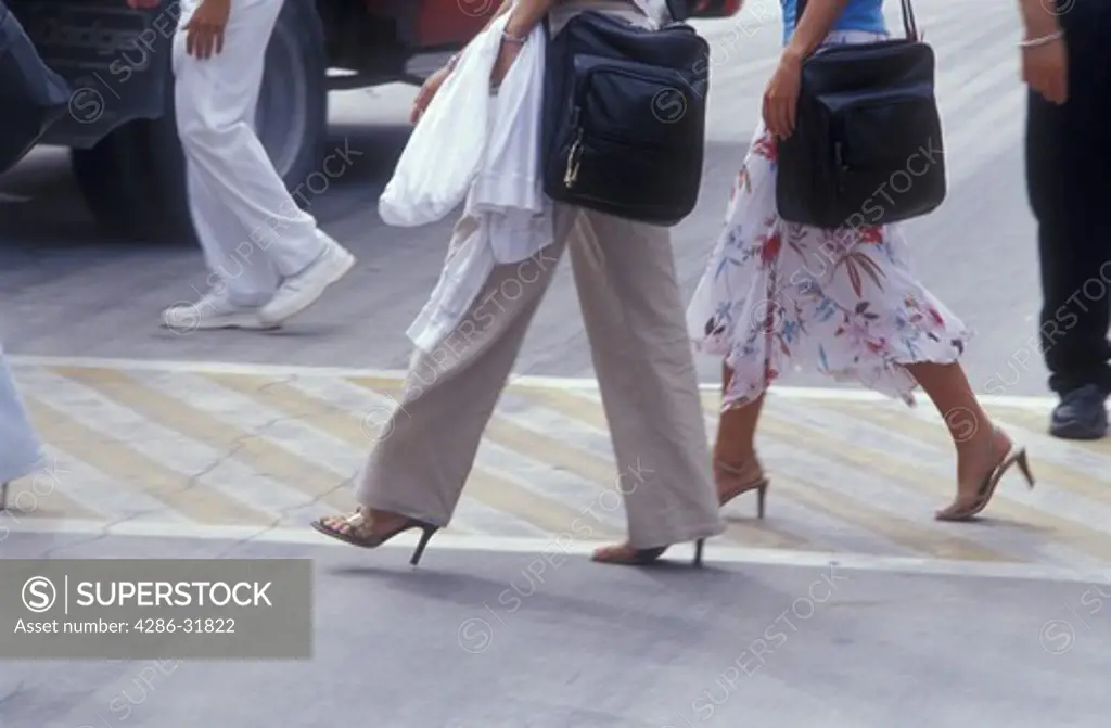 Close-up of two women's legs as they walk across a crosswalk at the Cozumel, Mexico airport.