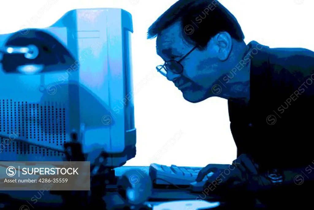 An Asian man squinting at a computer screen over his glasses while clicking his mouse.