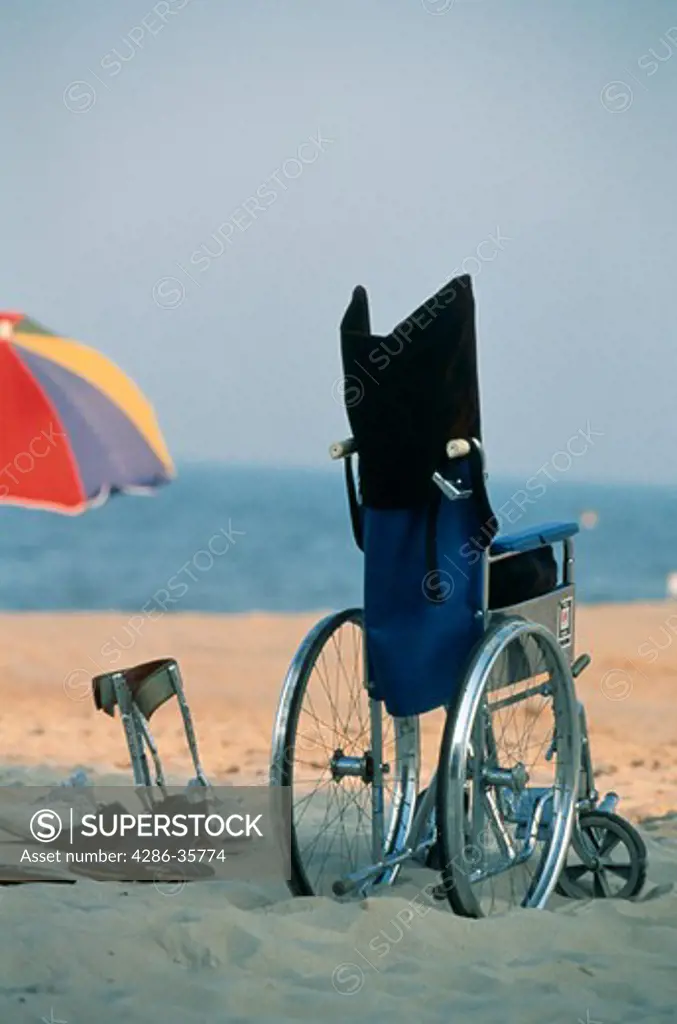 Beach scene, with wheelchair and legs braces, at a resort destination.  Large beach and umbrella file available. (Concept. Handicapped. Recreation.)