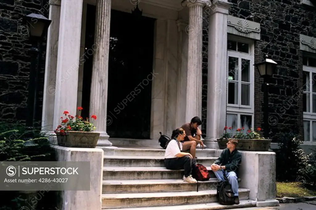 College students sitting on the steps of a campus building participating in campus related activities.