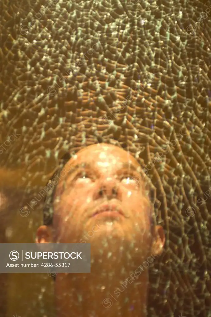 MIAMI, FLORIDA, USA - Man looks up, behind cracked glass. (MR)