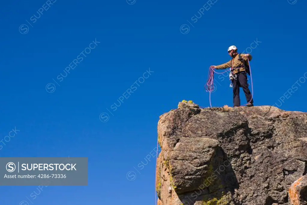  A mountaineer standing on top of a cliff coiling his climbing rope