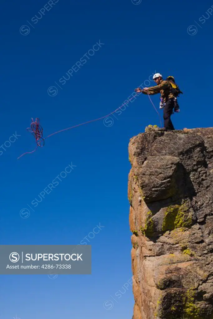  A mountaineer standing on top of a cliff throwing his climbing rope over the edge