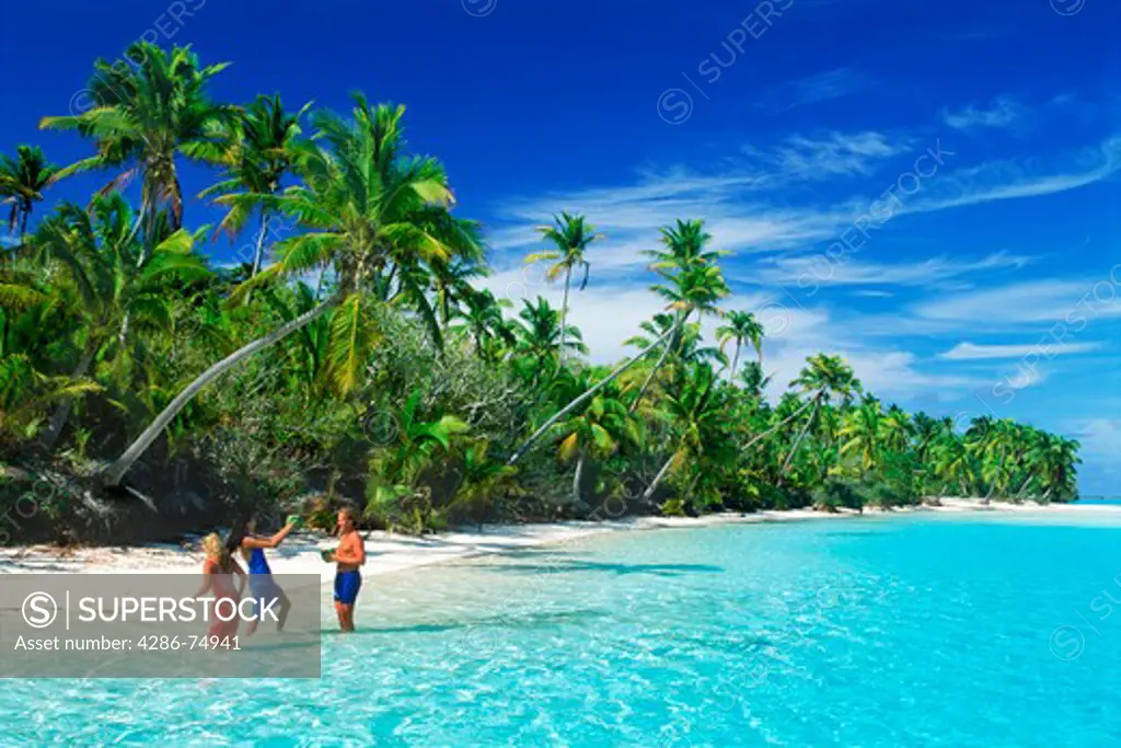 Tourists drinking from coconuts off One Foot Island in Aitutaki lagoon in Cook Islands