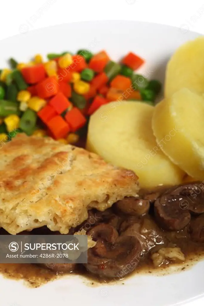 Vertical view of a meal of stewed kidneys topped with suet crust pastry and served with boiled potatoes and mixed vegetables