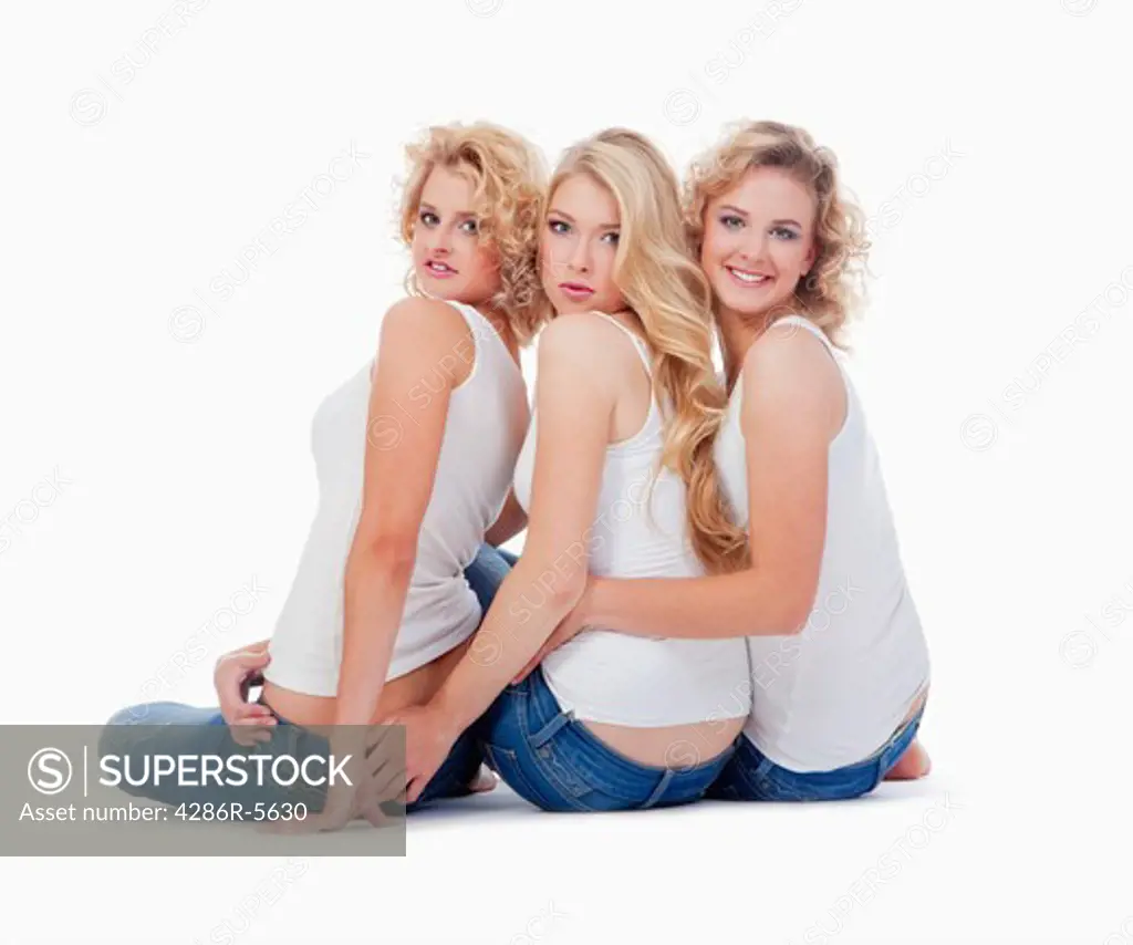 three young women sitting on the floor, looking up- isolated on white