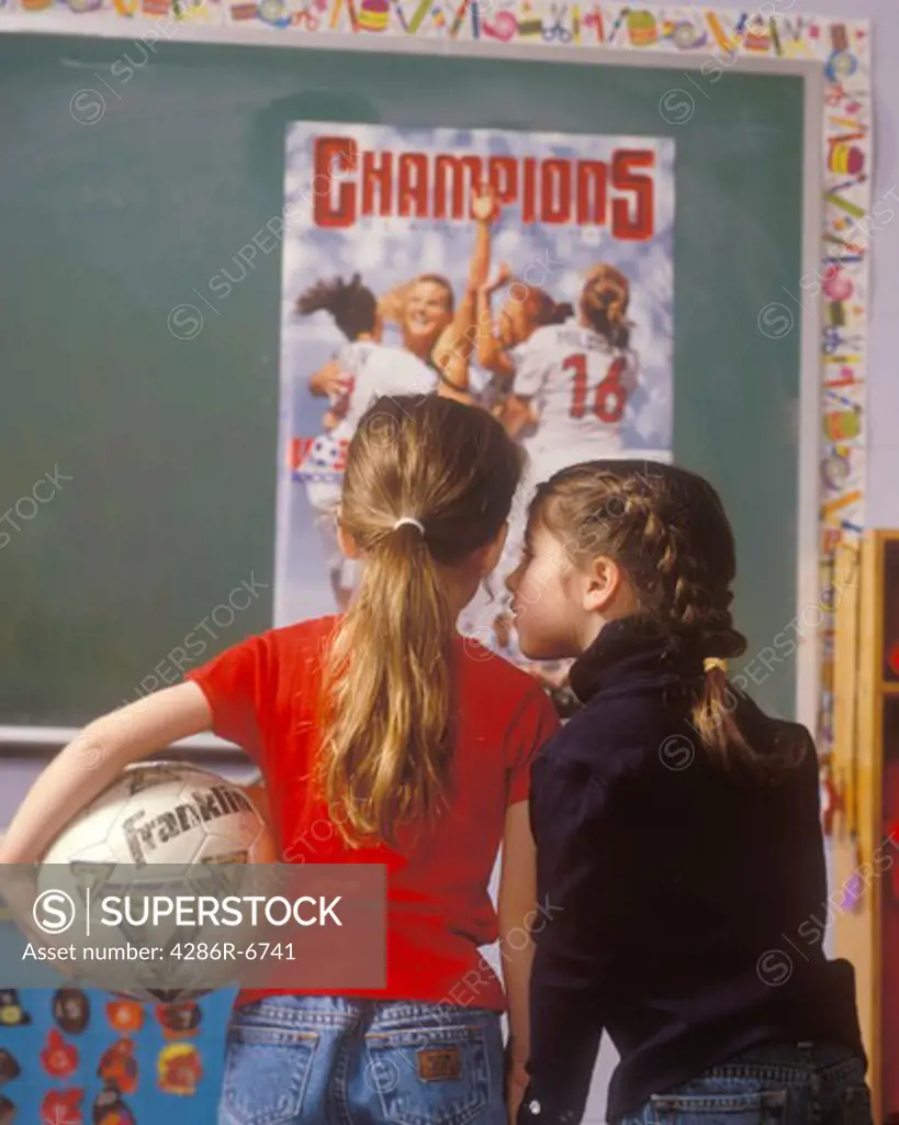 Two young girls with their backs to camera looking at a poster of the US Woman's Soccer team