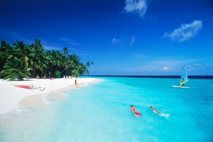 Couple snorkling in aqua waters with windsurfer at Fihalhohi Island in Maldives