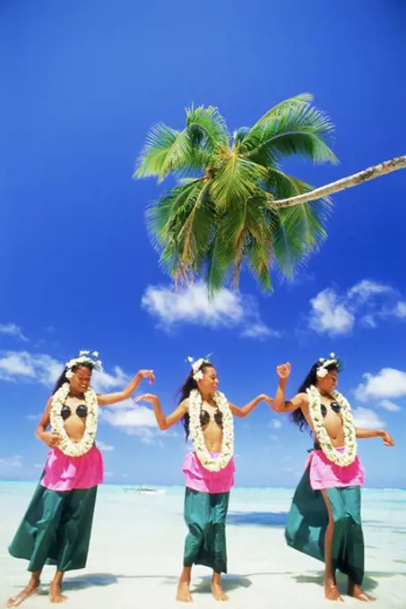 Three Polynesian girls with grass skirts and flower leis on Aitutaki Island in South Pacific