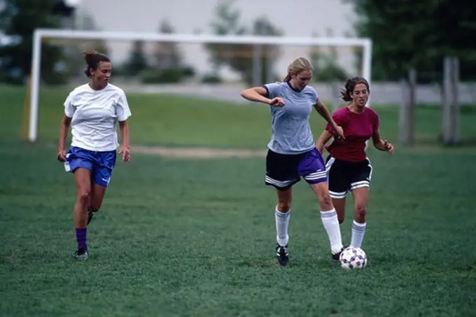 Three teenage girls energetically playing soccer.