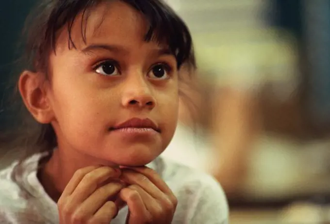 Close-up of a first grade latino girl with her hands under her chin. 