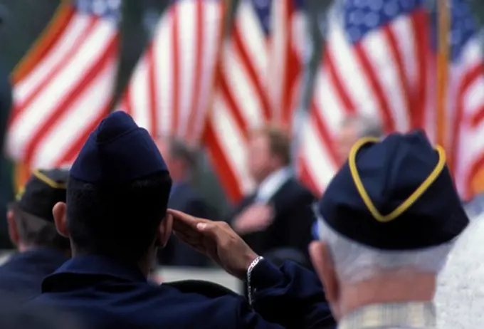 View from behind as veterans salute several American flags during a ceremony.