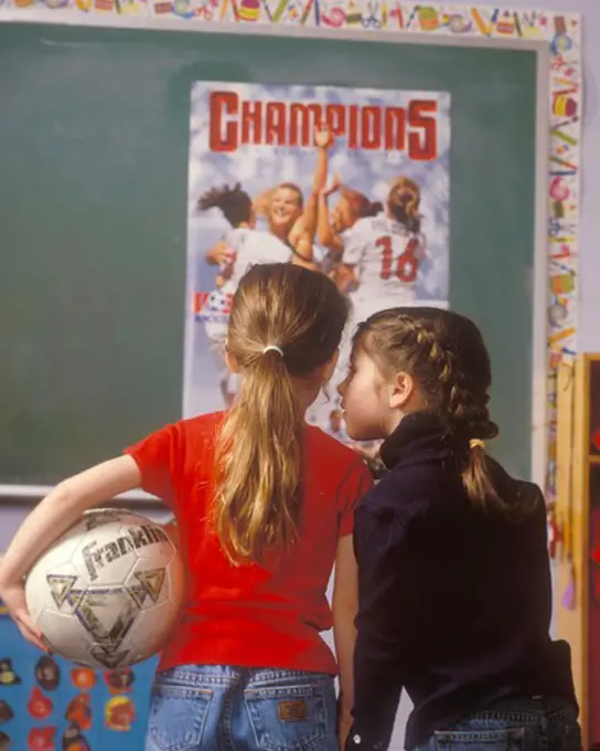 Two young girls with their backs to camera looking at a poster of the US Woman's Soccer team