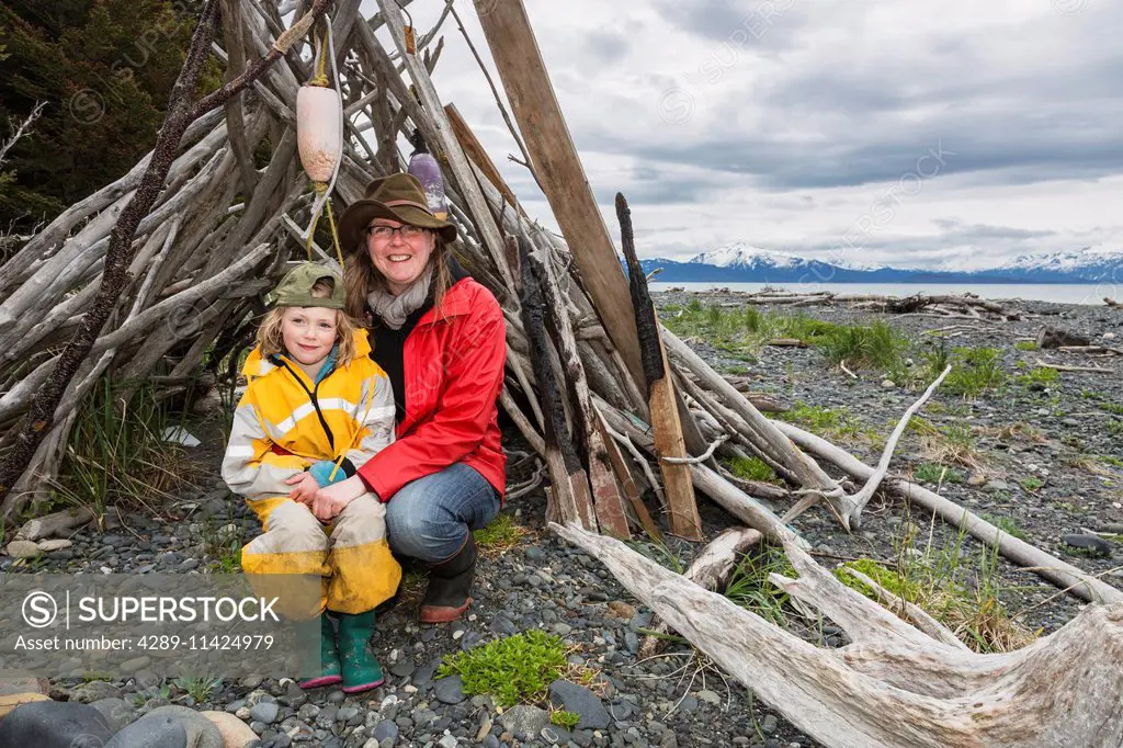 Mother and daughter pose in a driftwood shelter on Bishop's Beach, Homer, Southcentral Alaska, USA.