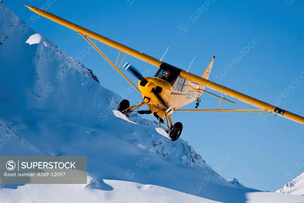 Yellow Piper Super Cub with wheel skis preparing to land on a glacier in the Neacola Mountains, Winter in Southcentral Alaska