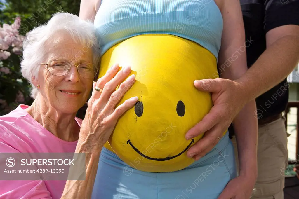 Pregnant woman posing with family with yellow Smiley Face painted on her stomach Alaska United States