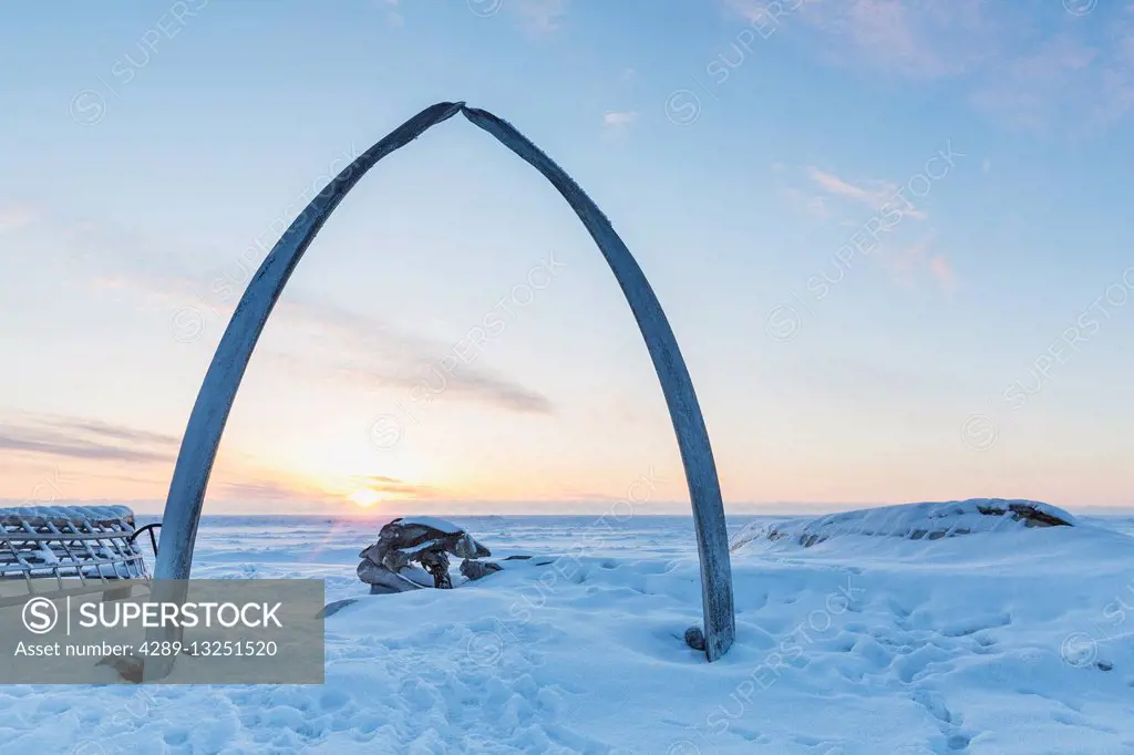 Whalebone arch frames the setting sun at the shore of the Arctic