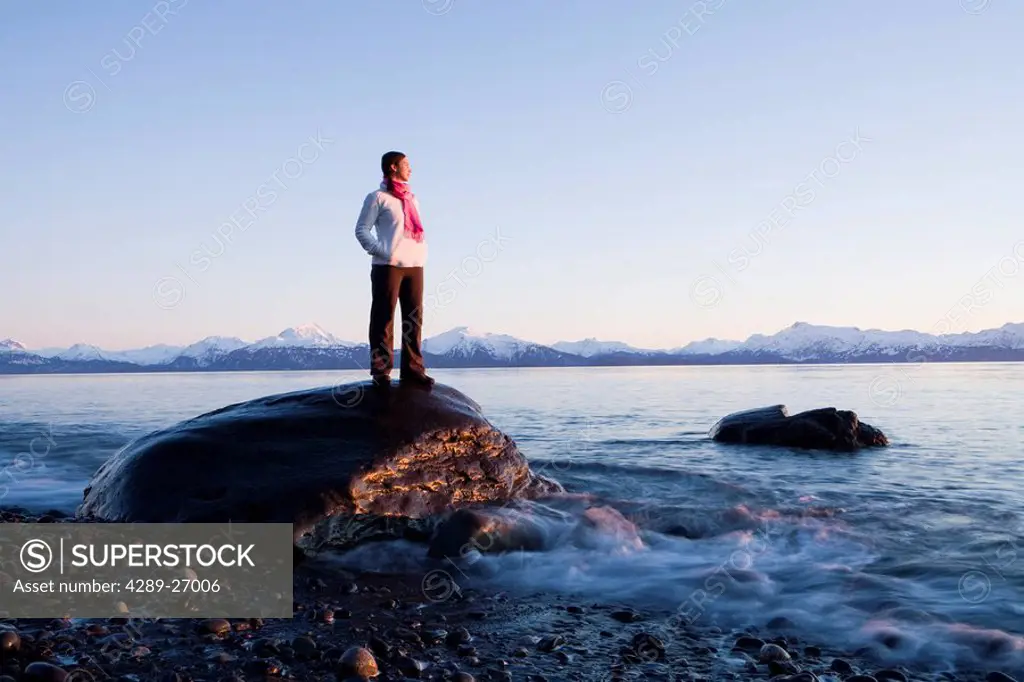 Woman stands on rock at Bishops Beach viewing Kachemak Bay at Homer, Alaska