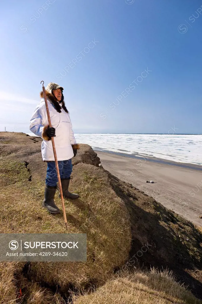 Portrait of a male Inupiaq Eskimo hunter wearing his Eskimo parka Atigi and seal skin hat and holding a walking stick at Old Utkeagvik original town s...