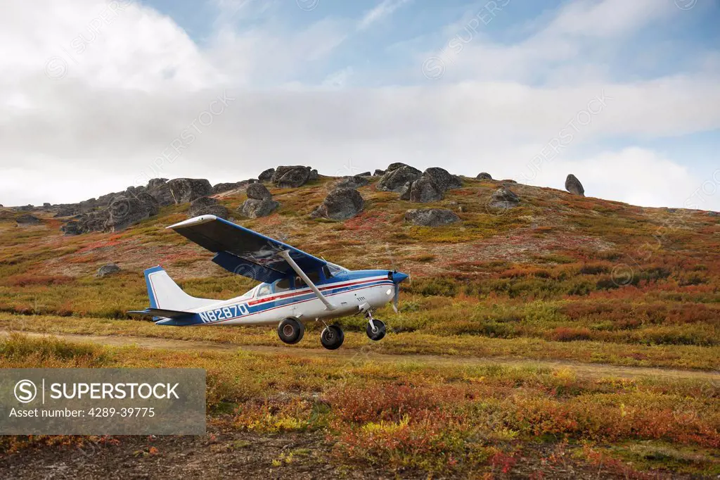 Cessna 206 bushplane takes off from a dirt airstrip at Serpentine Hot Sprints, with fall color on the tundra and granite tor rock formations, Bering L...