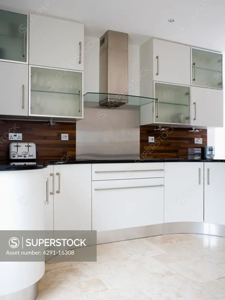 White and opaque glass wall cupbaords in modern white kitchen with black splashbacks and curved unit