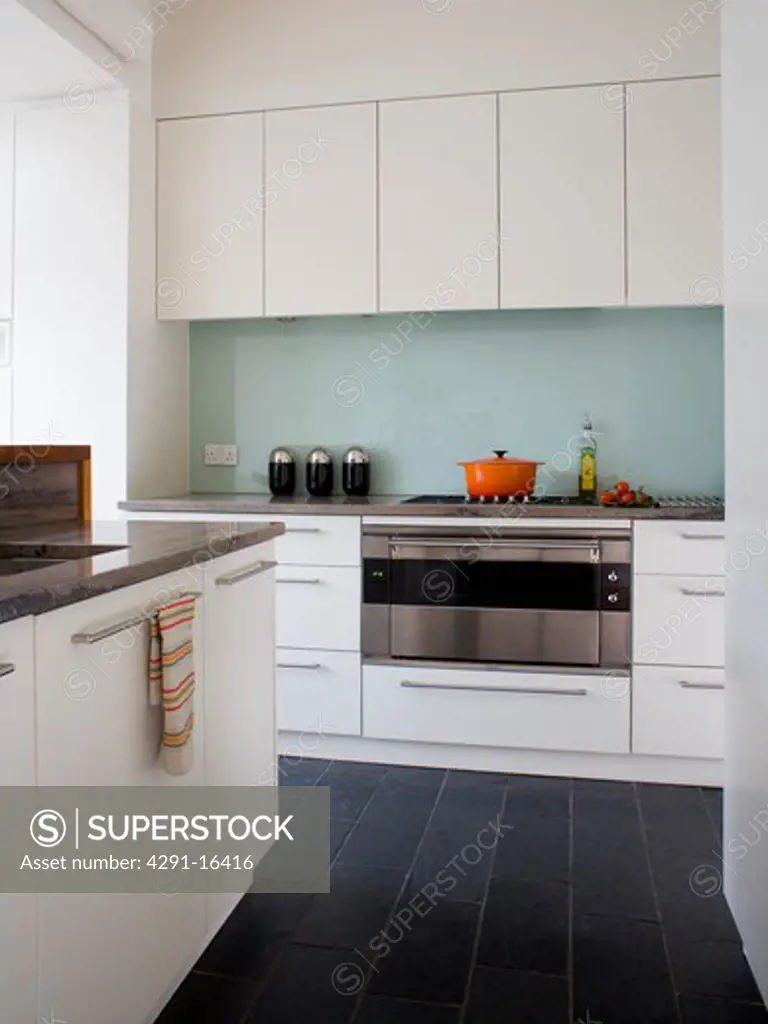 Black floor tiles in modern white kitchen with glass splashback behind stainless steel oven