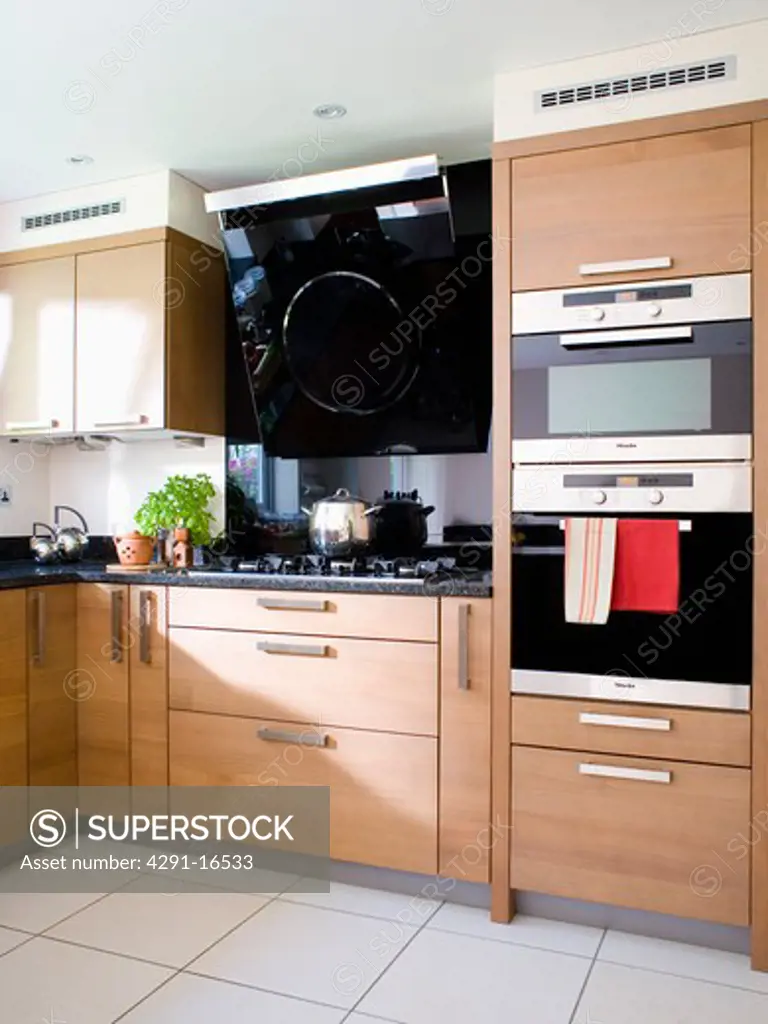 Double oven and gas hob in modern kitchen with pale wood fitted units