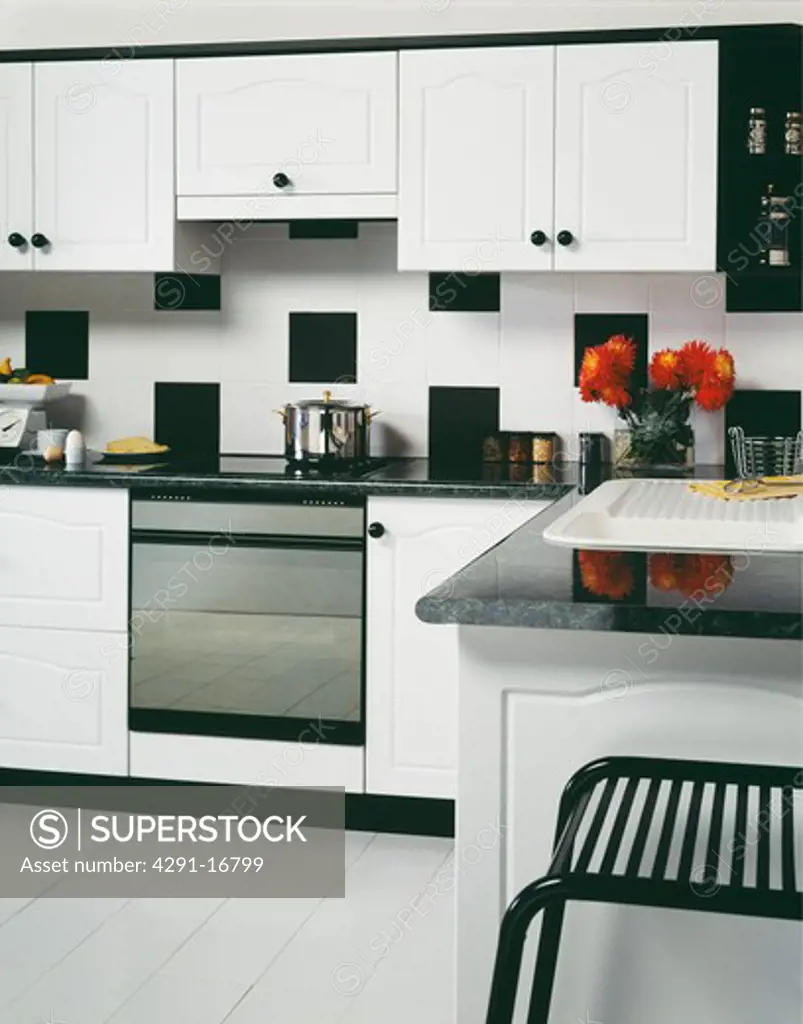 Large black and white tiles on wall above oven in modern white kitchen with white floor tiles