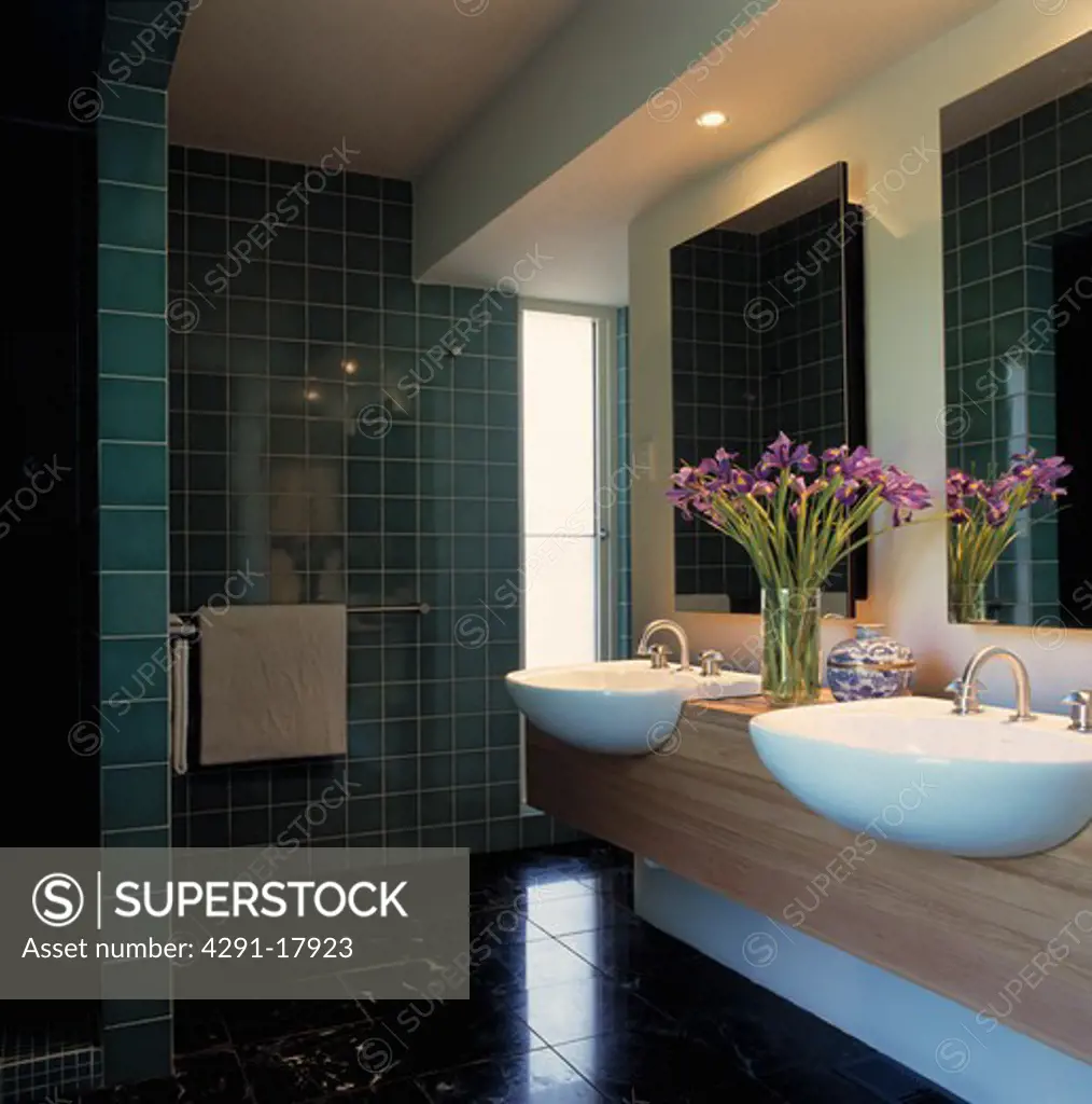 Double white basins in wooden vanity unit in modern bathroom with green wall tiles