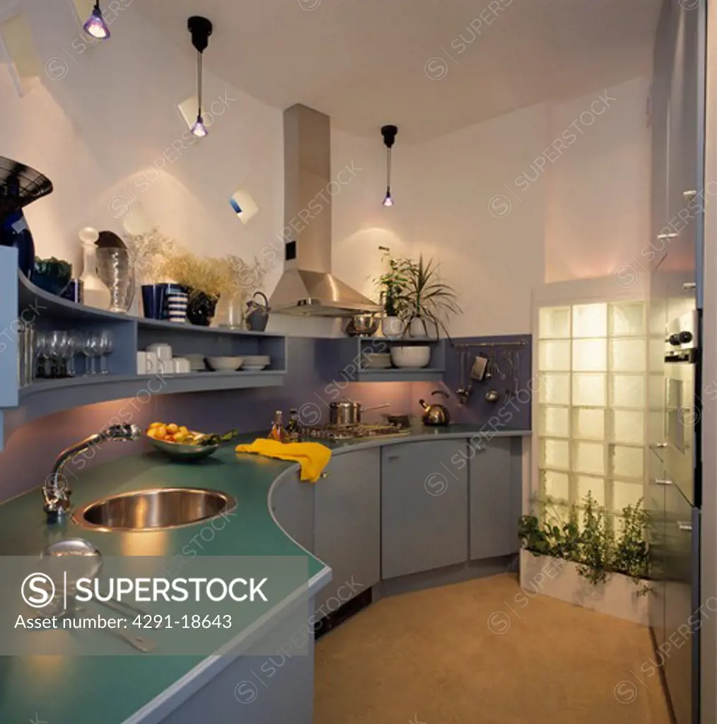 Circular stainless steel sink set into turquoise worktop above curved grey fitted cupboards in modern kitchen