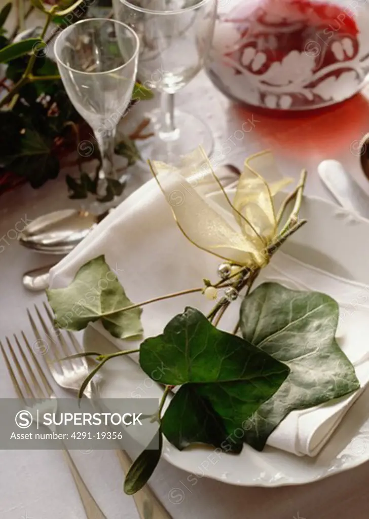 Close-up of green ivy leaves and sprig of mistletoe decorating white plate on Christmas dining table