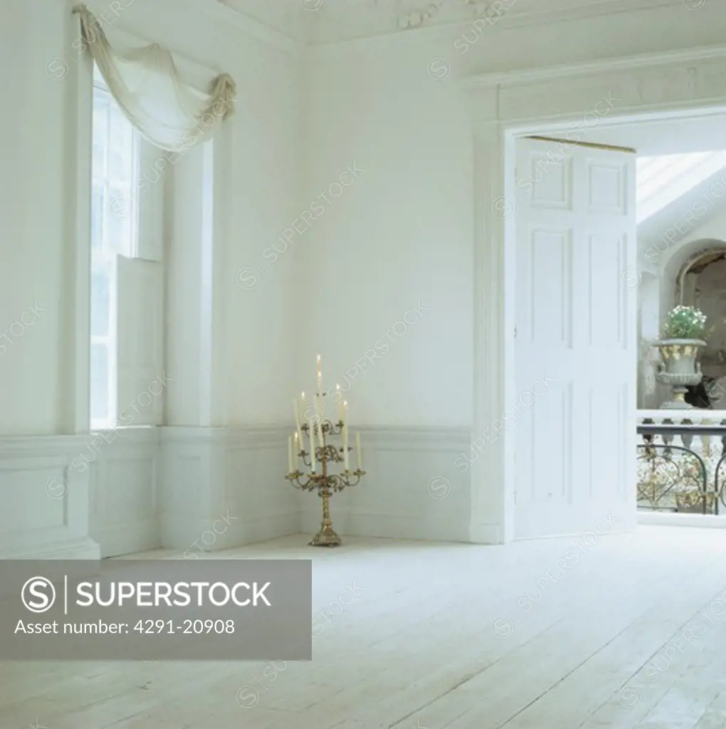 Ornate candlestick in empty white Georgian hall with white wooden floor and dado panelling